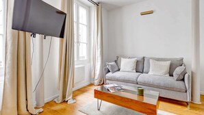 Un salon moderne avec un téléviseur à écran plat fixé au mur, un canapé gris agrémenté de coussins, une table basse en verre et un plancher en bois.