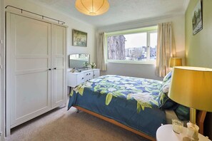 Un dormitorio con cama, cómoda, espejo, ventana con cortinas y lámpara.