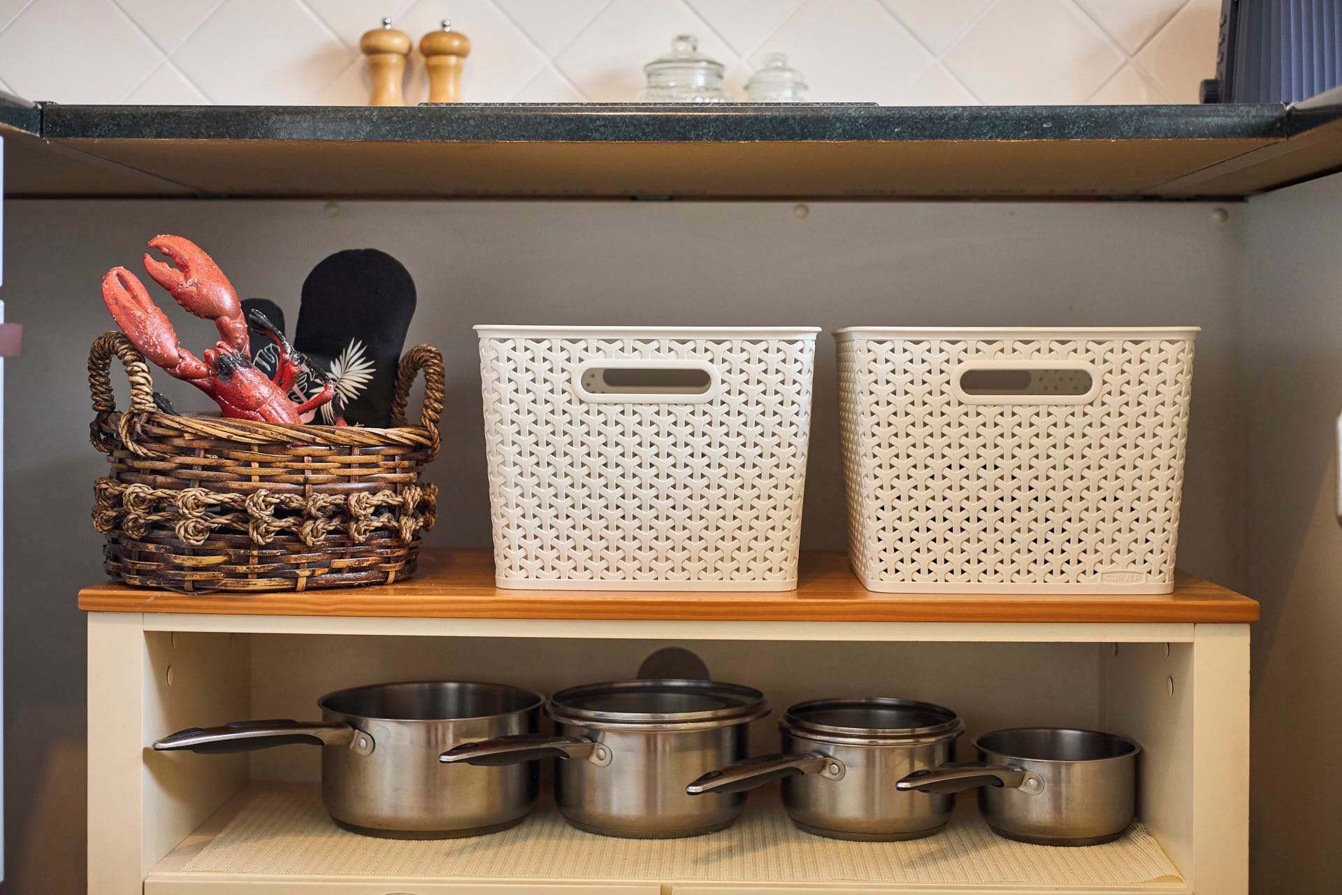 Une étagère de cuisine avec deux paniers en plastique blanc et un panier en osier contenant des ustensiles de cuisine.