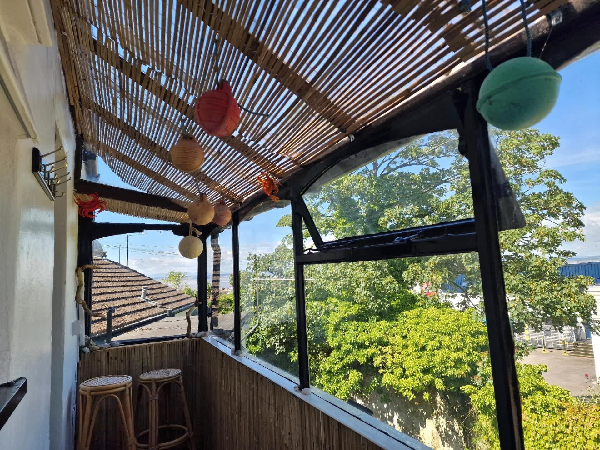 Une pièce avec un plafond en bambou, une grande fenêtre donnant sur les arbres et deux tabourets en osier.