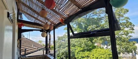 Una habitación con techo de bambú, un ventanal con vista a árboles y dos taburetes de mimbre.