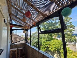 A room with a bamboo ceiling, a large window with a view of trees, and two wicker stools. - Host & Stay | Beachcomber Cottage Apartment (Morecambe)