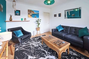 Un salon avec un canapé en cuir noir, une table basse en bois et un tapis à motifs noir et blanc.