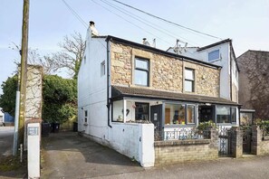Une maison à deux étages avec une façade en pierre, un porche à l’avant doté d’une balustrade et une porte de garage visible.