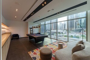 A modern living room with a pool table, a sofa, and a large window offering a city view. - Stunning 1 Bedroom Burj Khalifa View (Dubai)