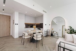 A modern kitchen with white cabinetry, a dining area with a round table and chairs, and a living area with a sofa and a glass coffee table. - Stunning 1 Bedroom Burj Khalifa View (Dubai)