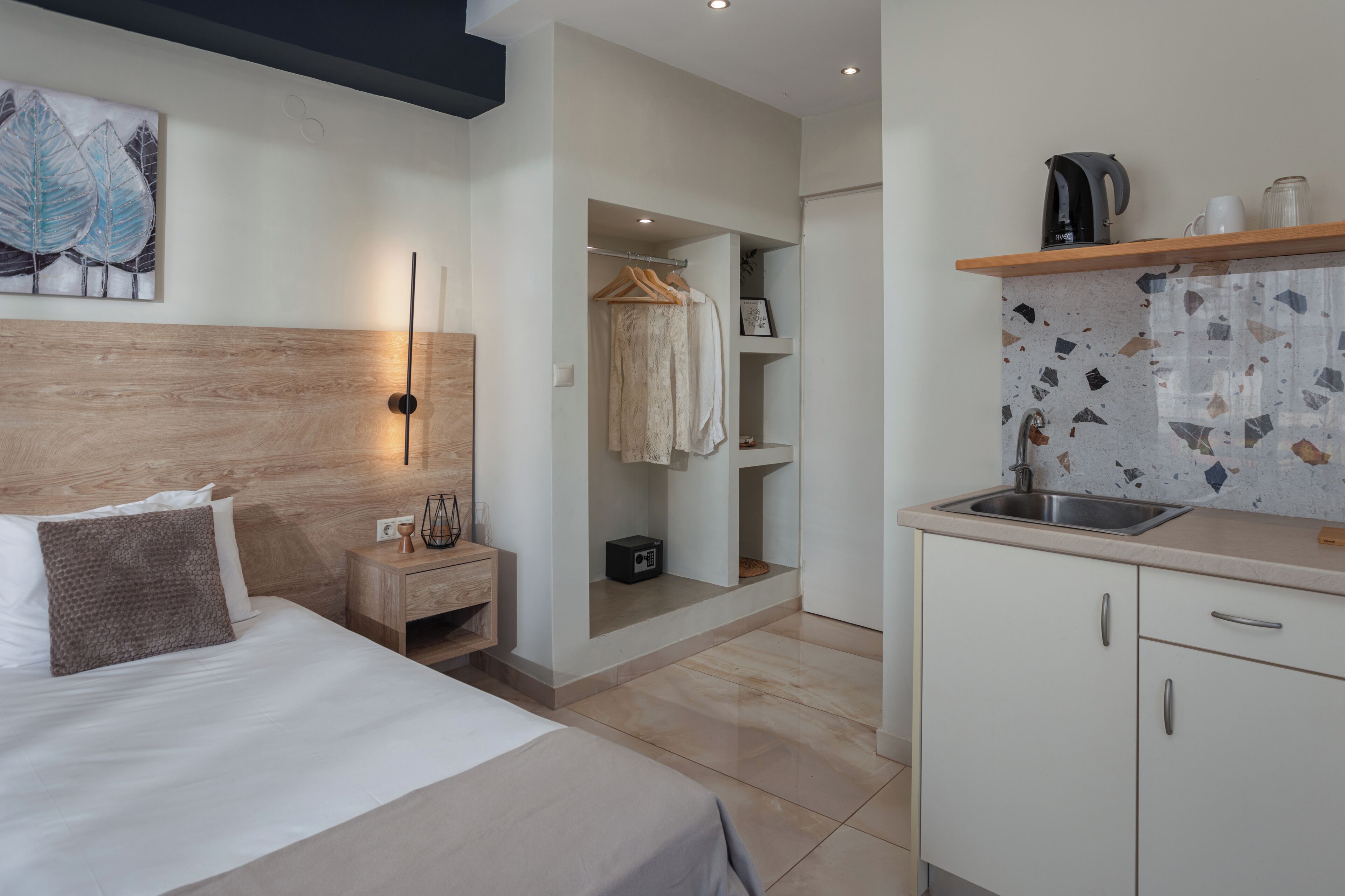 Una habitación de hotel moderna con cama, mesita de noche y una pequeña kitchenette.