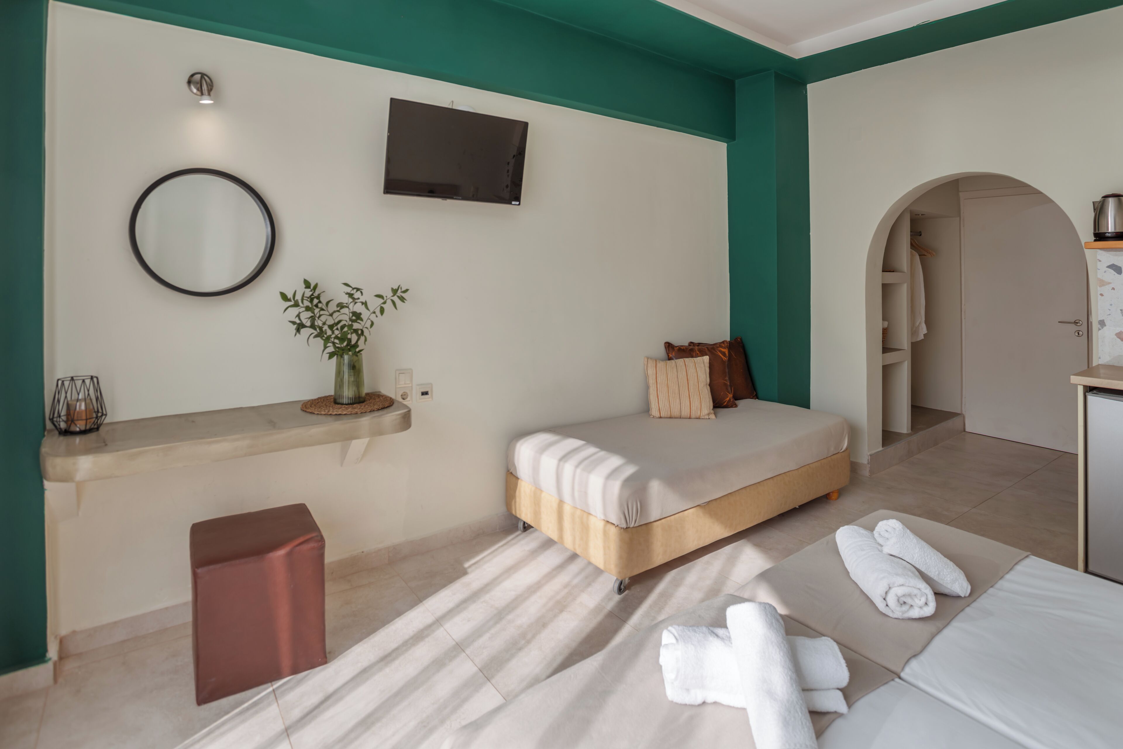 A bedroom with a bed, a TV mounted on the wall, a small plant, and a mirror.