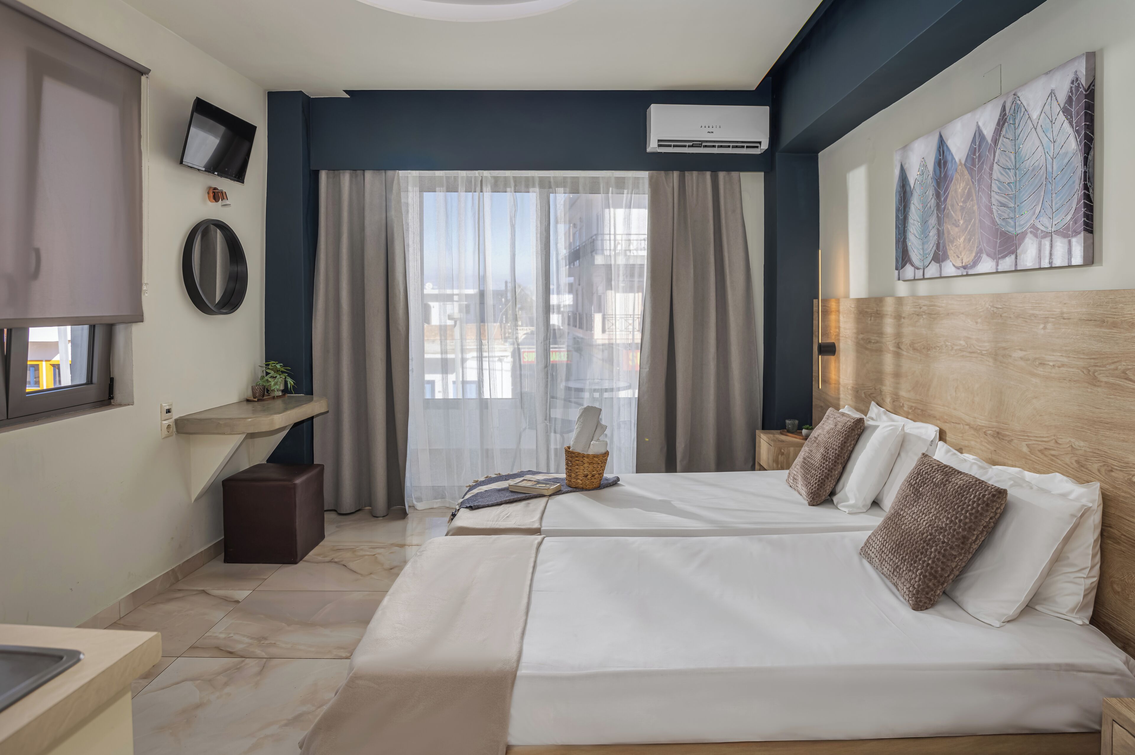 A hotel room with a large bed, a TV, an air conditioning unit, a window with curtains, and a wall-mounted artwork.