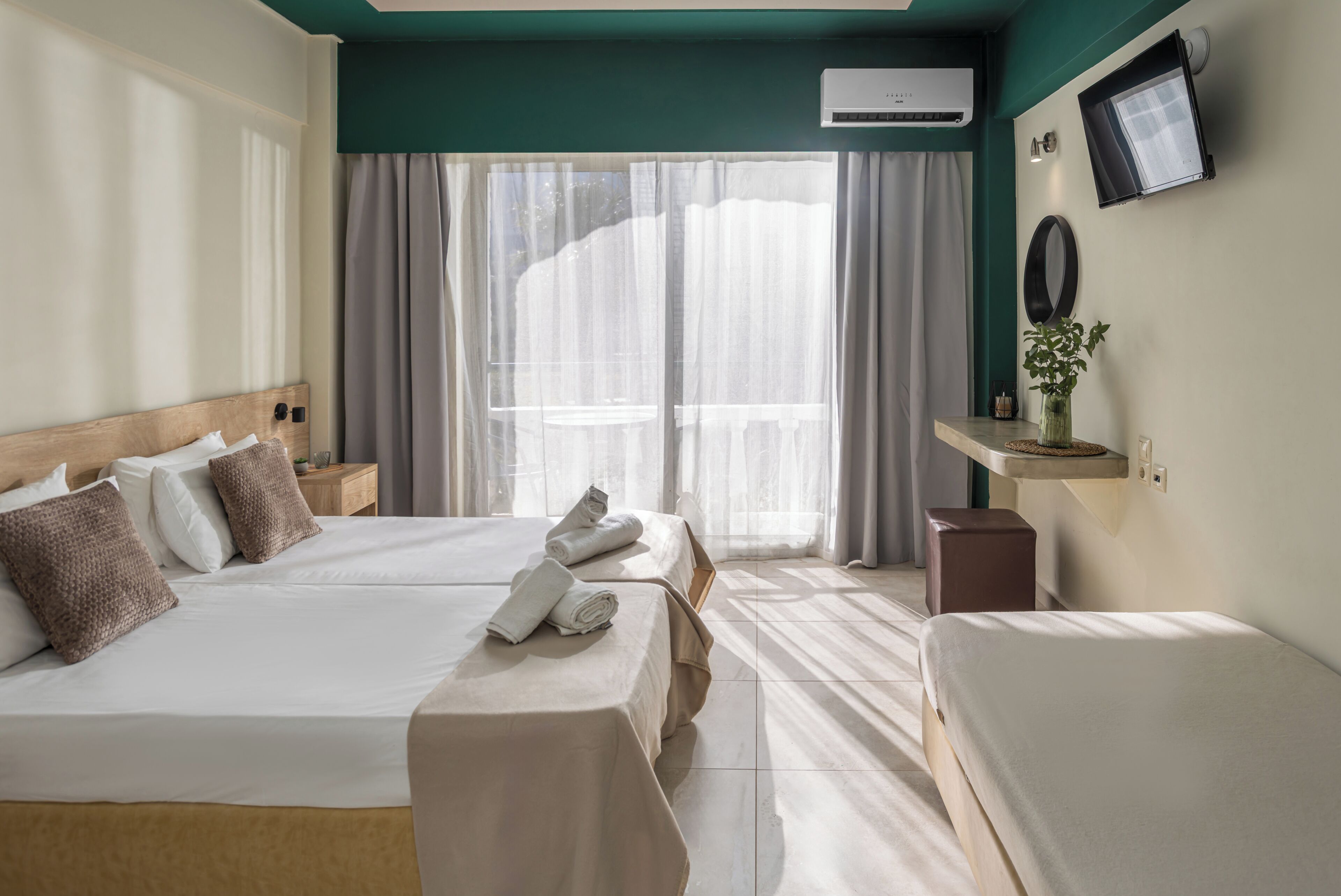 A hotel room with two beds, a TV, a small table with a vase, and a window with curtains.