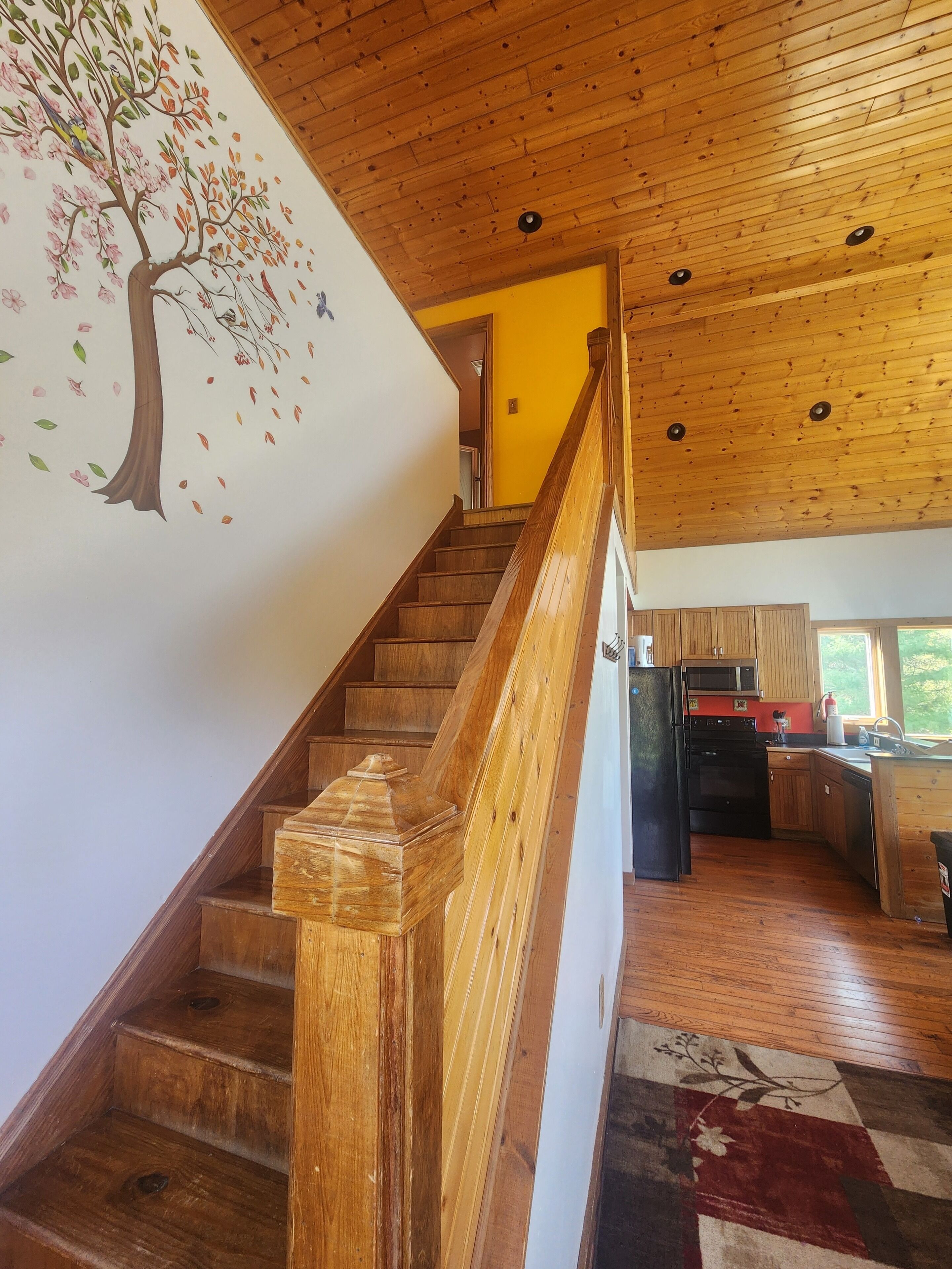 A wooden staircase leading to a kitchen with a wooden ceiling and a wall mural.