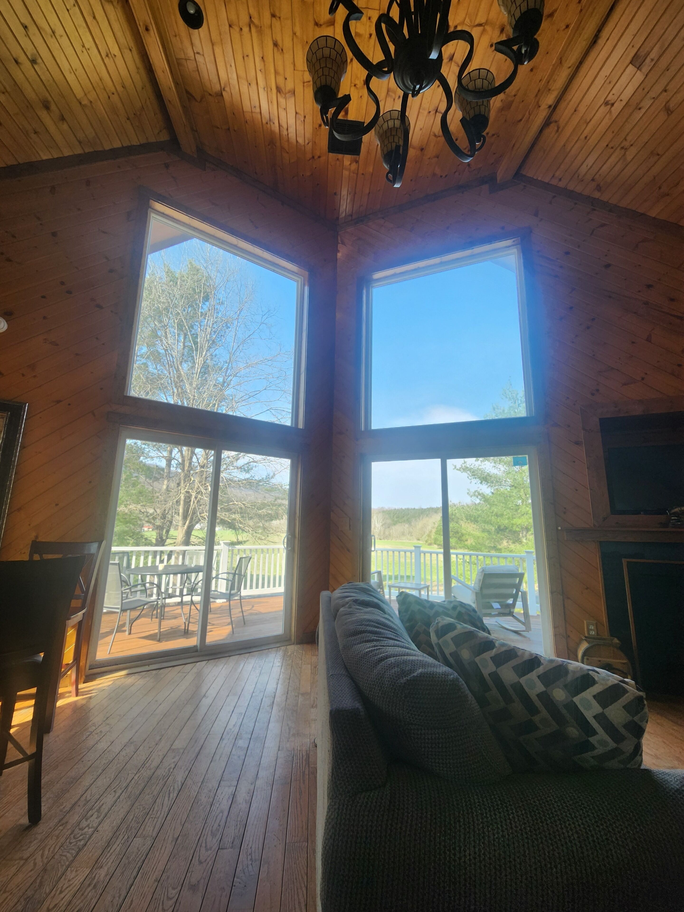 A cabin interior with a large window, a sofa, a television, and a wooden ceiling.
