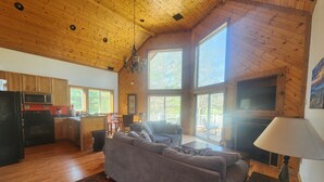 Un salón espacioso con techo de madera, un sofá, una mesa de comedor y una zona de cocina.