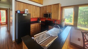 Una cocina con armarios de madera, un refrigerador negro, un microondas y un lavamanos.
