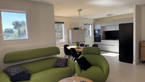 Ein modernes Wohnzimmer mit einem grünen Sofa, einem Esstisch und einer Küchenzeile mit einem schwarzen Kühlschrank.