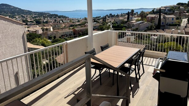 Ein Balkon mit Tisch und Stühlen, mit Blick auf eine Küstenstadt mit Häusern und Meer.