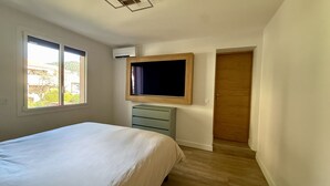 Ein Schlafzimmer mit Bett, Schminktisch, Wandfernseher und einer Tür.