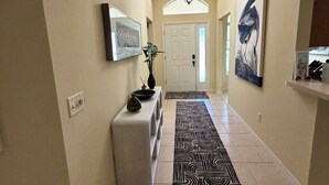 A hallway with a patterned rug, a white bench, a wall-mounted TV, and a door at the end. - Beautiful 3-bedroom house on private cul-de-sac with Golf Cart in The Villages (The Villages)