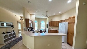 A modern kitchen with a central island, wooden cabinets, a white refrigerator, and a ceiling fan. - Beautiful 3-bedroom house on private cul-de-sac with Golf Cart in The Villages (The Villages)
