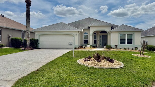 A residential house with a garage, a driveway, and a well-maintained lawn with landscaping. - Beautiful 3-bedroom house on private cul-de-sac with Golf Cart in The Villages (The Villages)