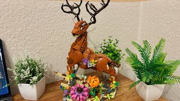 A LEGO deer sculpture with flowers and plants on a wooden surface.