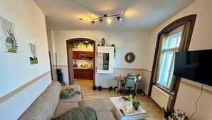A living room with a sofa, a coffee table, a TV, and a kitchen in the background. - Görlitzer Zweisamkeitsquelle, Bezauberndes Wohnung mit ausgestatteter Küche (Görlitz)
