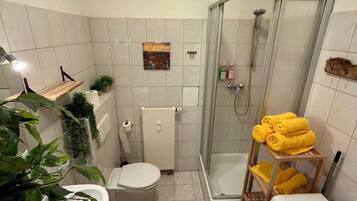 Een kleine badkamer met toilet, douche en wasmachine.