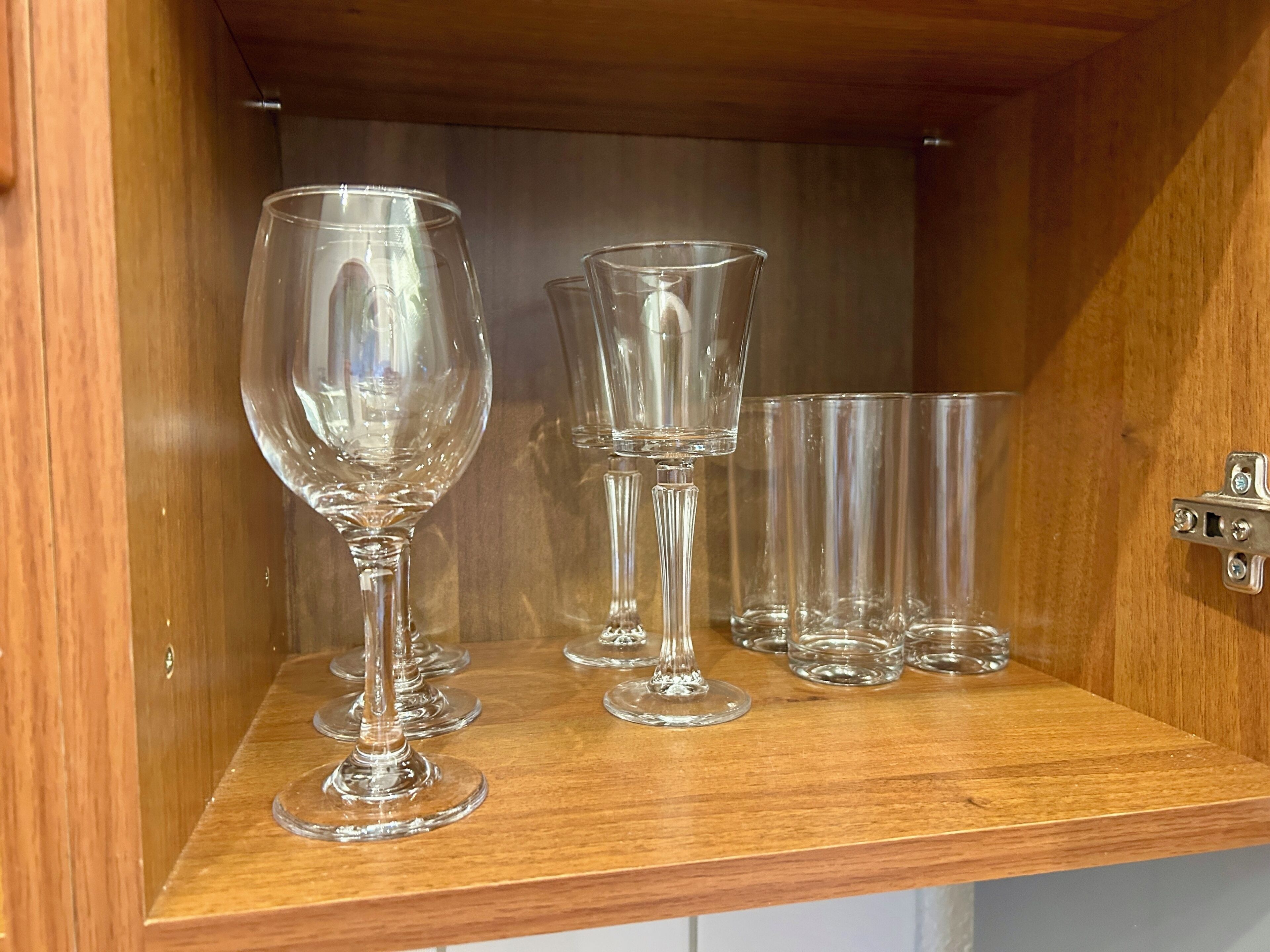 Un meuble en bois muni d’une étagère où sont rangés plusieurs verres à vin en verre transparent.