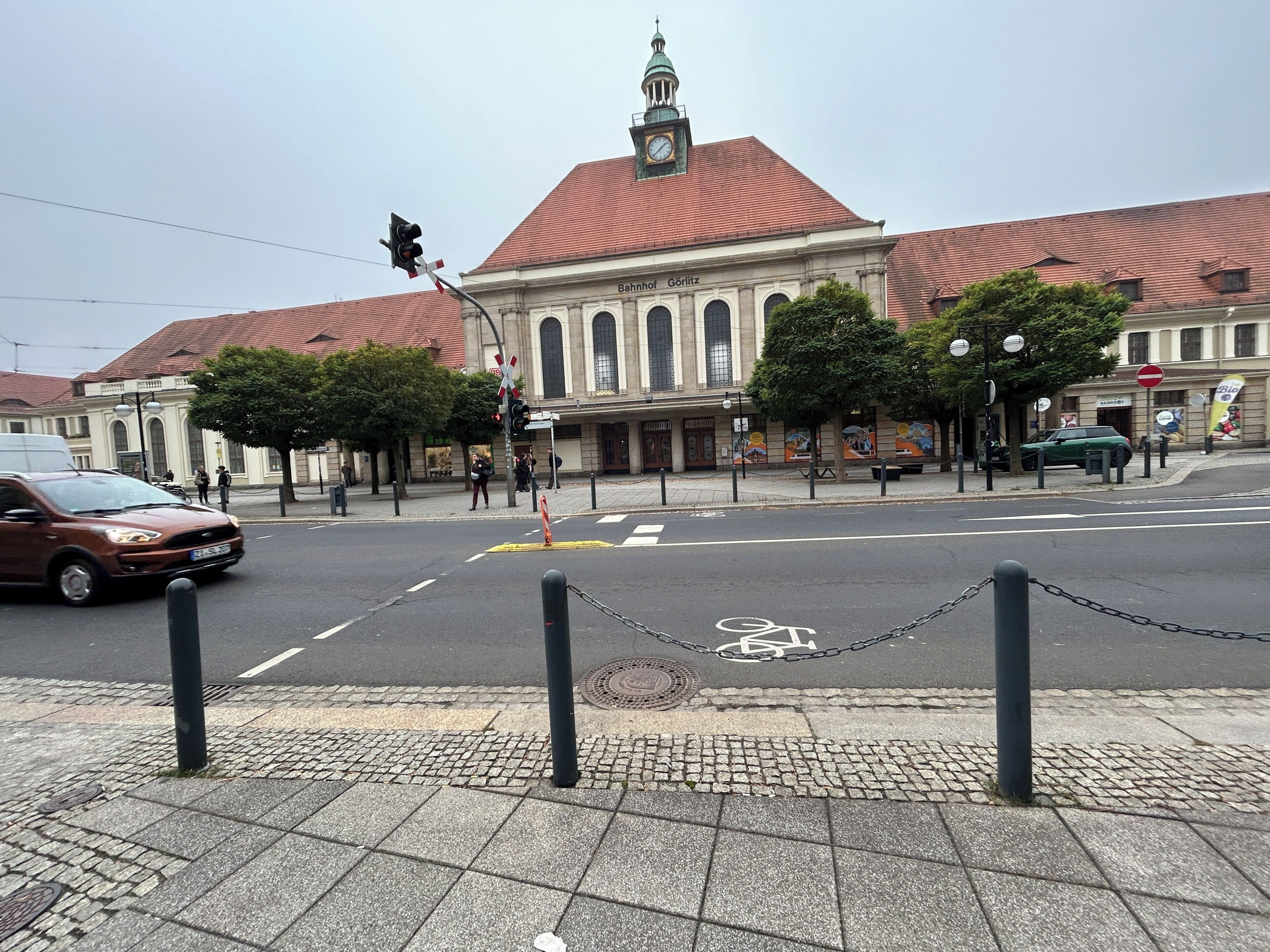 A street view with a building featuring a clock tower and a red roof.