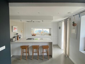 A modern kitchen with a central island, bar stools, pendant lighting, and a view of a car through the window. - Duplex apartment in Bidart - walk to the beach and forest (Bidart)