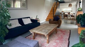 Una sala de estar moderna con un sofá azul oscuro, una mesa de centro de madera y una escalera que lleva a una zona de cocina.