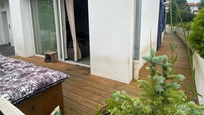 Un edificio moderno con terraza de madera, puerta corredera de vidrio que da a una habitación y una pequeña zona de estar al aire libre.