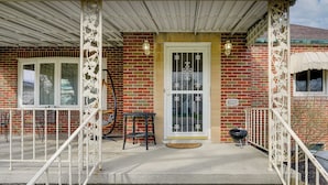 A brick building with a white porch, a door with decorative glass, and a small table. - 1 Mi to Dtwn Tiffin! Brick Bungalow w/ Patio, Yard (Tiffin)