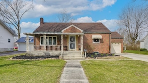 A two-story brick house with a front porch, a garage, and a well-maintained lawn. - 1 Mi to Dtwn Tiffin! Brick Bungalow w/ Patio, Yard (Tiffin)