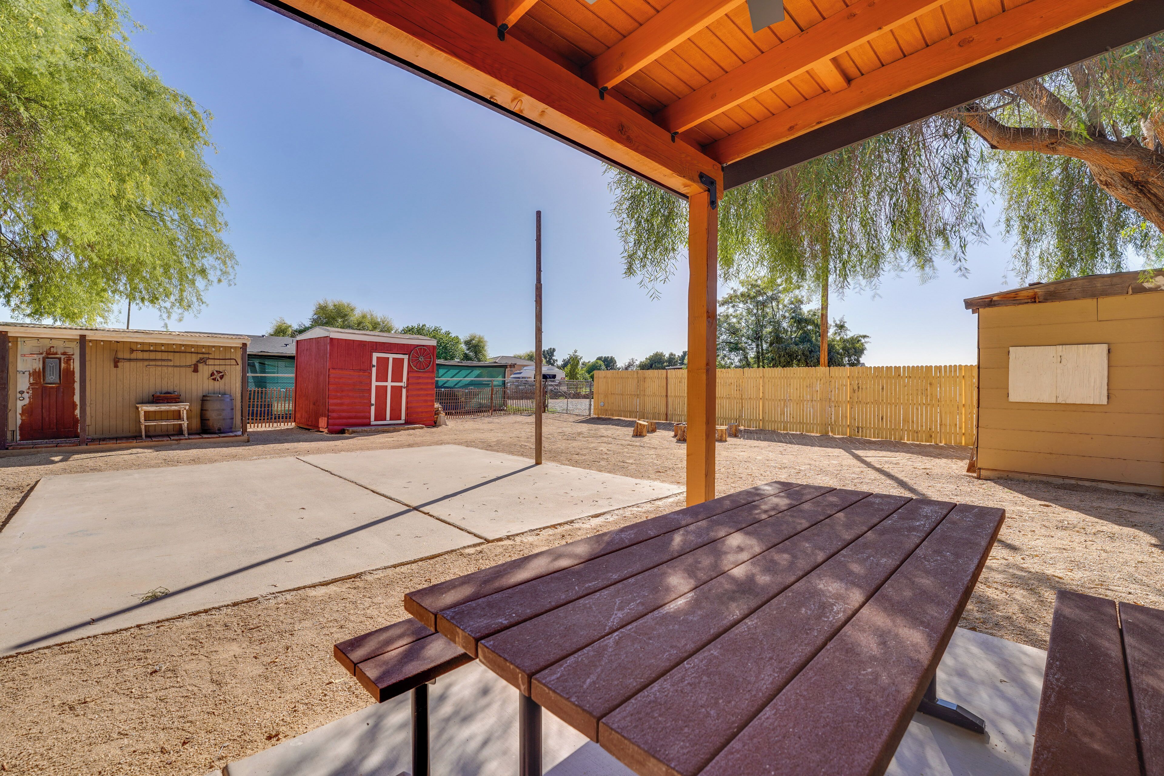 An outdoor patio with picnic tables, a covered area, and a fenced yard with buildings.