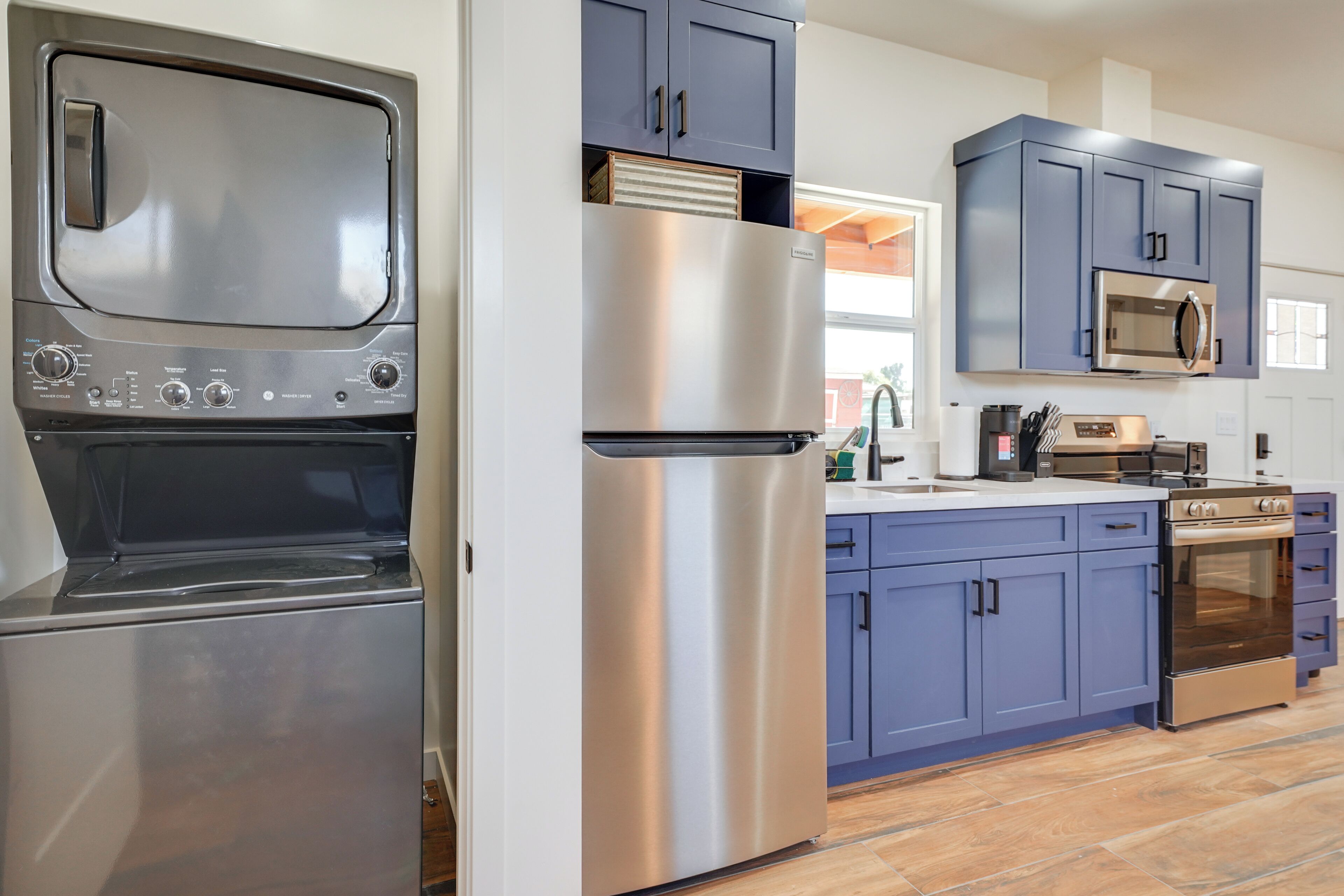A kitchen with stainless steel appliances, blue cabinets, and a wooden floor.