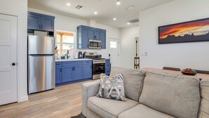 A modern kitchen with blue cabinets, a stainless steel refrigerator, and a dining area with a gray sofa and a painting of a sunset. - Outdoor Space, Near Everything: Glendale Getaway! (Glendale)