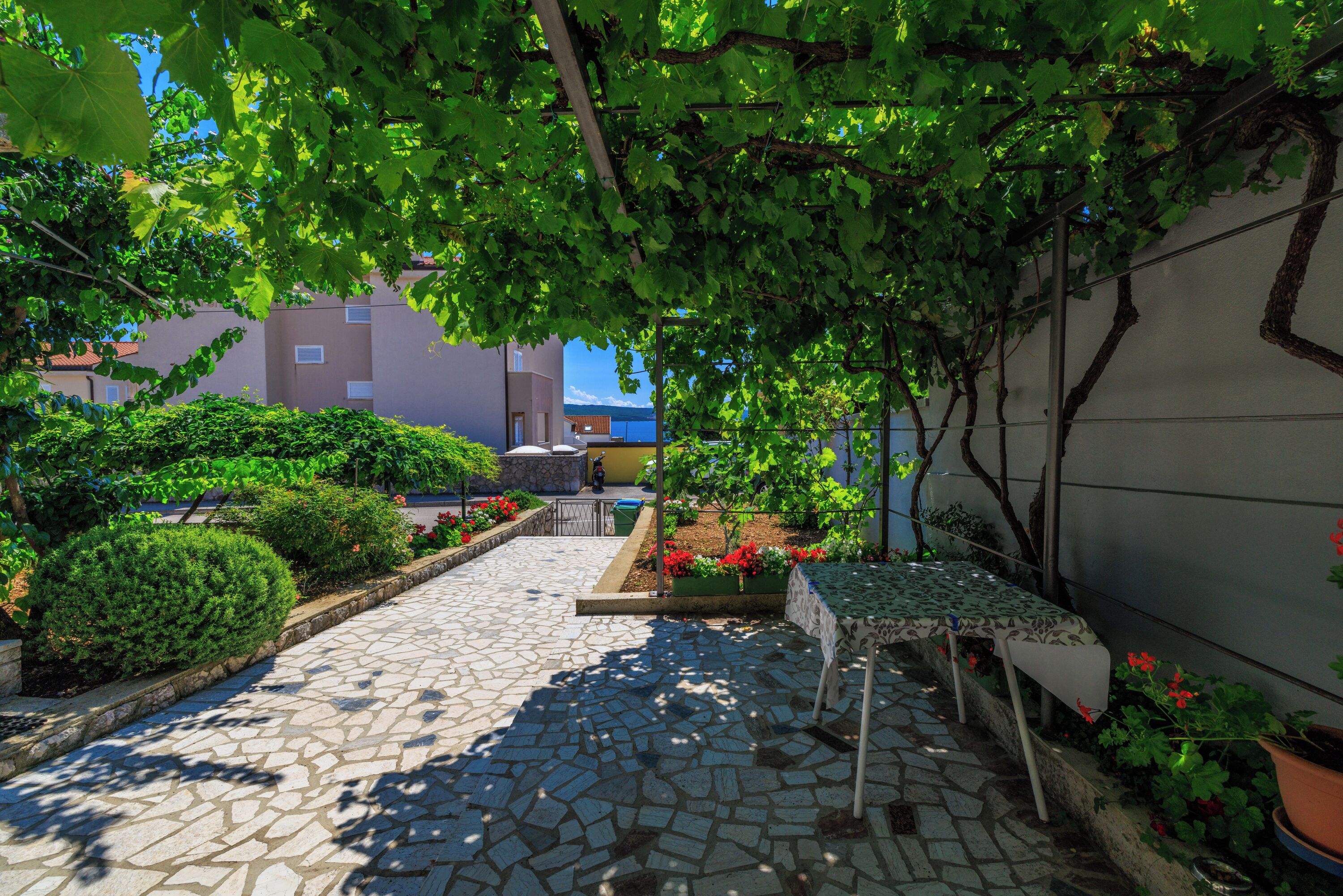 Un cortile con un vialetto in pietra, piante in vaso e un tavolo con sedie.