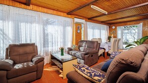 Una sala de estar amoblada con techo de madera, un sofá, un sillón reclinable y un comedor con mesa y sillas.