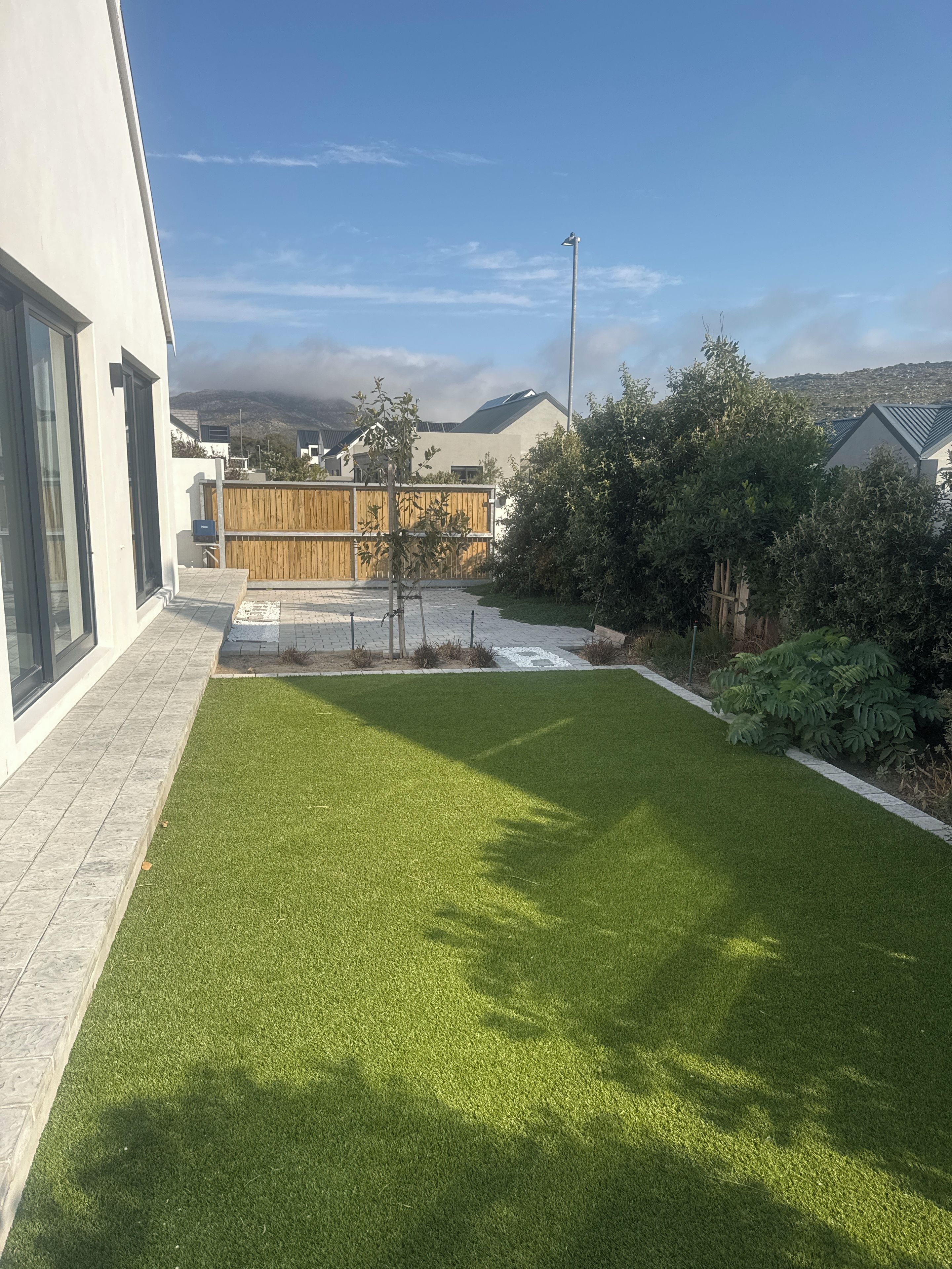 A modern residential property with a well-maintained lawn, a wooden fence, and a view of a hilly landscape.