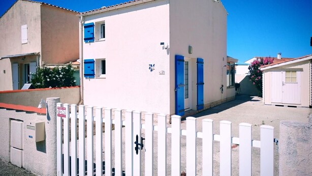 Un bâtiment à deux étages, doté d’une façade blanche, de portes bleues et d’une antenne parabolique.