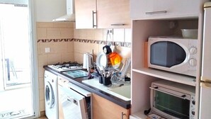 Une cuisine compacte équipée d’un lave-linge, d’un four à micro-ondes et d’un four traditionnel.