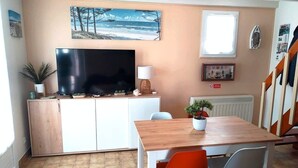 Une pièce avec un téléviseur, une table à manger, des chaises, une plante en pot et une fenêtre.