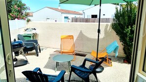 Une terrasse avec des meubles d’extérieur, un barbecue et un parasol vert.