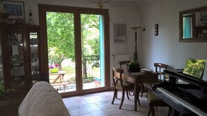 A living room with a piano, a dining table with chairs, a sofa, and a sliding glass door leading to a garden. - Guest Room 'Chambre T' with Shared Terrace & Garden, Wi-Fi Included (Saint-Rémy-lès-Chevreuse)