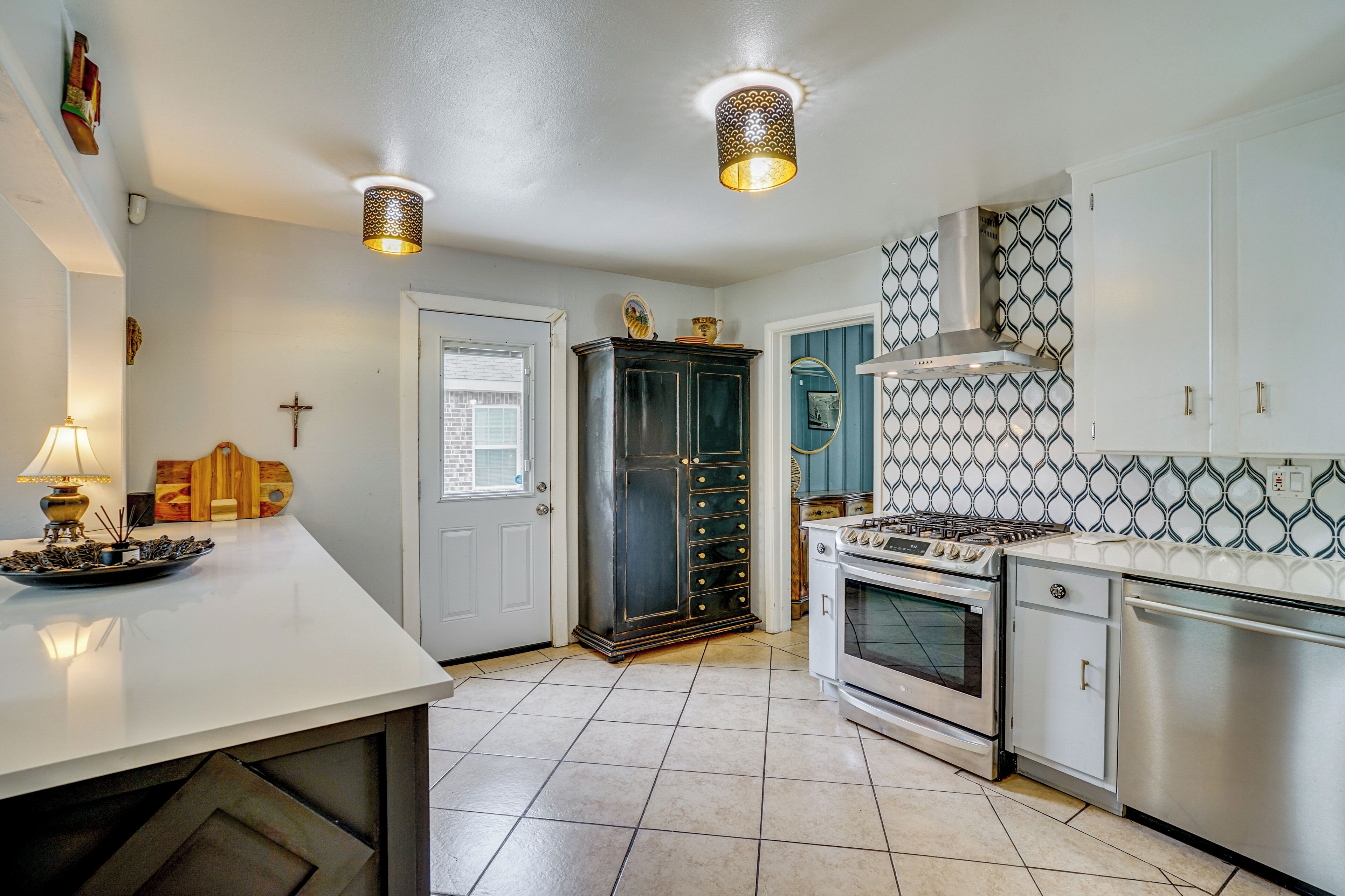 A kitchen with a white countertop, stainless steel appliances, patterned backsplash, and a cabinet with multiple drawers.