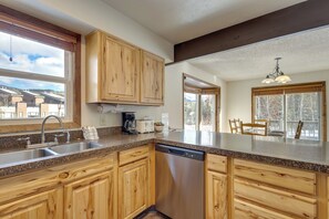 A kitchen with wooden cabinets, a dishwasher, a sink, and a window overlooking a residential area. - Steps From Ski Shuttle! WP Condo w/ Heated Pool (Winter Park)