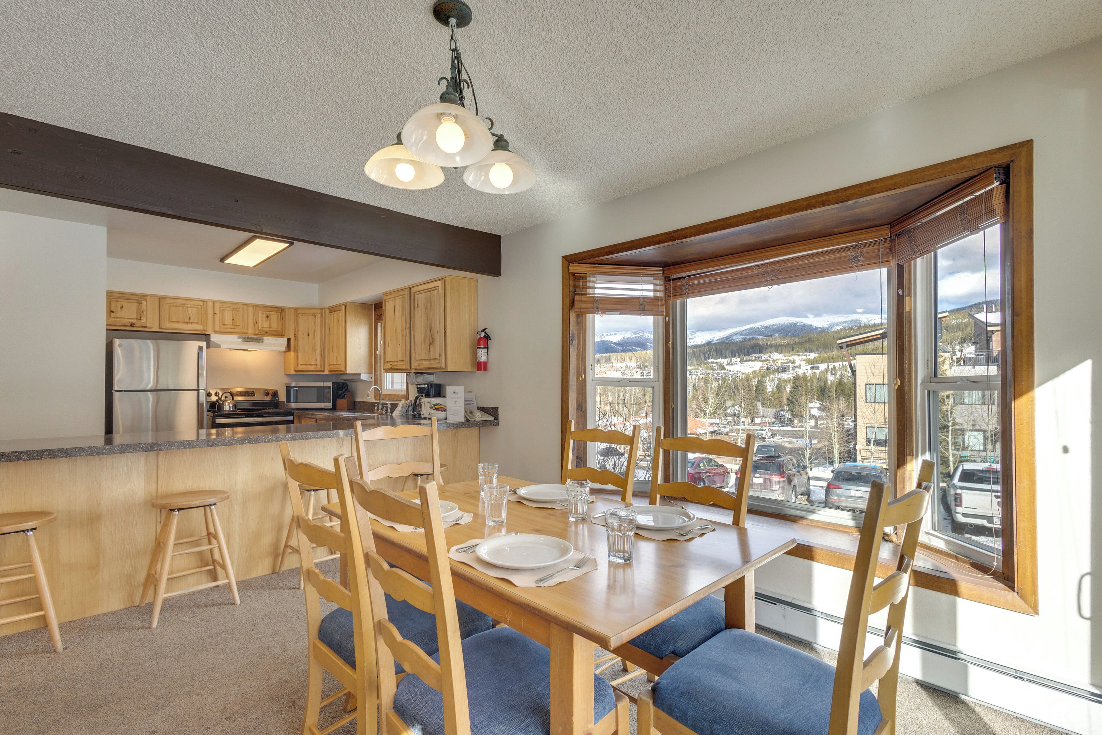 A modern kitchen with wooden cabinets, a central island, and a dining area with blue cushioned chairs.
