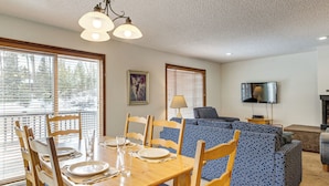 A dining area with a wooden table set for four, a sofa, and a television in a living room. - Condo 3 Mi to Winter Park Resort: Community Perks! (Winter Park)