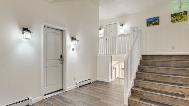 A hallway with a white door, a staircase, and wall-mounted light fixtures. - Condo 3 Mi to Winter Park Resort: Community Perks! (Winter Park)